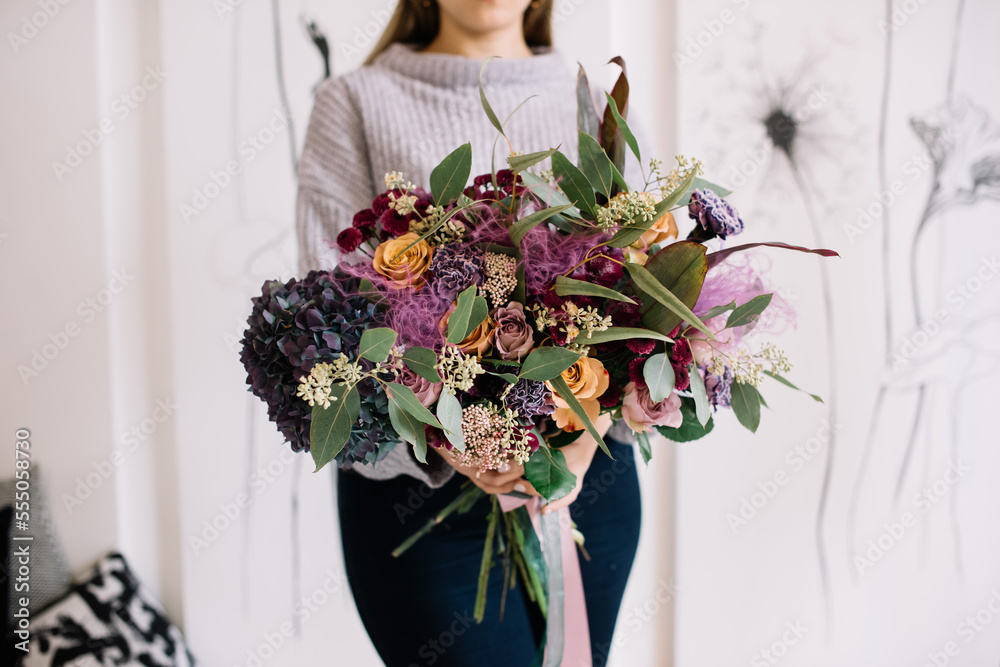 Very nice young woman holding big and beautiful bouquet of fresh hydrangea, roses, eucalyptus, carnations flowers in purple and blue colors, cropped photo, bouquet close up