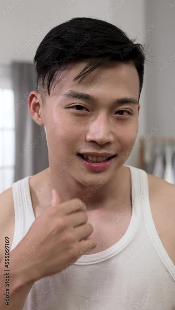 Vertical Video: shoulder shot smiling Korean male looking at camera like mirror combing hair and satisfied with his perfect facial skin while getting ready for the day at home. Vertical Video: shoulder shot smiling Korean male looking at camera like mirror combing hair and satisfied with his perfect facial skin while getting ready for the day at home.