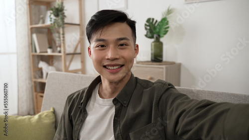 happy Taiwanese young male facing the camera is having an online video chat in the living room at home.