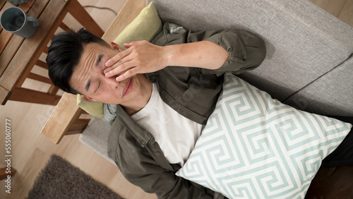 view from above of a sleepy asian young man lying on sofa after yawning rubbing eyes at home. photo