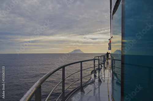 Stromboli volcano at horizon with clouds of smoke coming from summit seen from outdoor deck of luxury cruiseship cruise ship liner during Mediterranean cruising at twilight