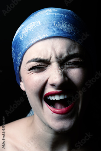 Fashion and make-up concept. Beautiful woman with screaming facial expression and scarf on her head. Close-up studio portrait. Model with closed eyes looking at camera. Toned image with blue color