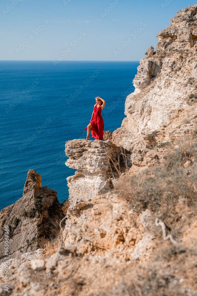 A woman in a red flying dress fluttering in the wind, against the backdrop of the sea.
