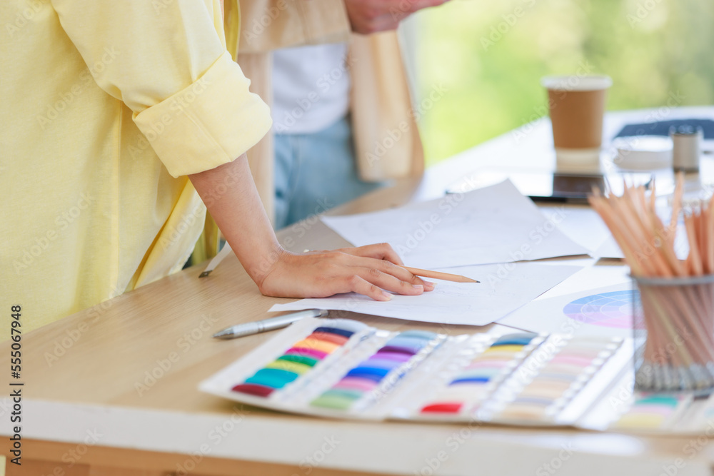 Closeup shot of colorful thread pattern collection placed on working table while unrecognizable professional dressmaker designer seamstress talking discussing together with colleague in tailor studio