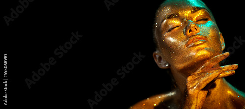 Fashion model woman skin face in bright gold sparkles, colorful neon lights, beautiful sexy girl portrait. Trendy glowing gold skin make-up. Art design make up. Glitter metallic shine golden makeup