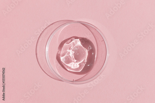 Hyaluronic acid serum or gel for the face in Petri dish on a pink background. Concept of cosmetics laboratory researches, wellness and beauty. Cosmetic texture. Top view