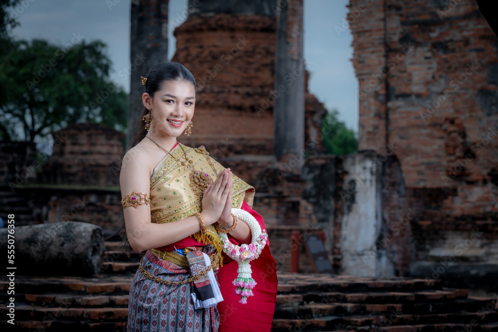 Portrait Asian model posing to pay respect with smiling wearing Thai dress traditional costume and flower  greeting thai culture with ancient famous background. 
