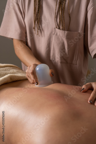 Close-up of a masseur doing a back massage using a silicone vacuum jar. Cupping treatment for the treatment of back pain in a young woman. Concept of health, body care. Vertical photo