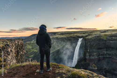Young man standing and looking at Majestic Haifoss waterfall flowing in volcanic canyon among the Icelandic Highlands on summer at Iceland