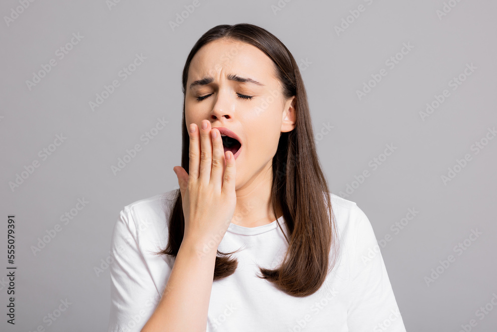 Close up shot selective focus portrait of yawn young woman holds hand near open mouthed tired woman after hard exhausted day at work standing on grey background. Close up shot selective focus portrait of yawn young woman holds hand near open mouthed tired woman after hard exhausted day at work standing on grey background.