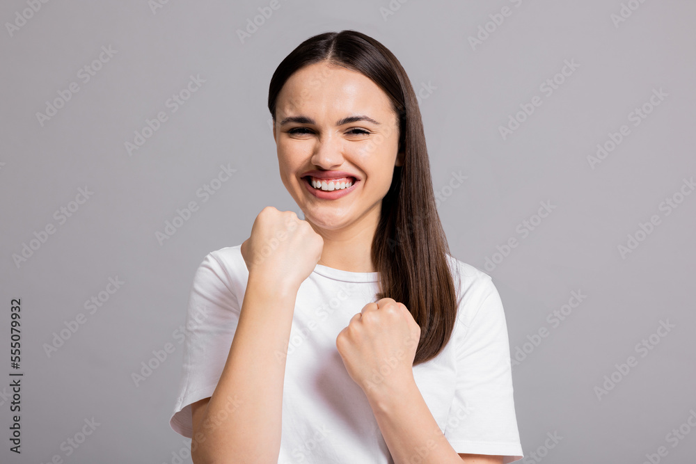 Portrait of young attractive adorable lovely pretty cute successful cheerful woman winning celebrating isolated on grey background wearing casual white t-shirt showing delighted emotions at camera. Portrait of young attractive adorable lovely pretty cute successful cheerful woman winning celebrating isolated on grey background wearing casual white t-shirt showing delighted emotions at camera.