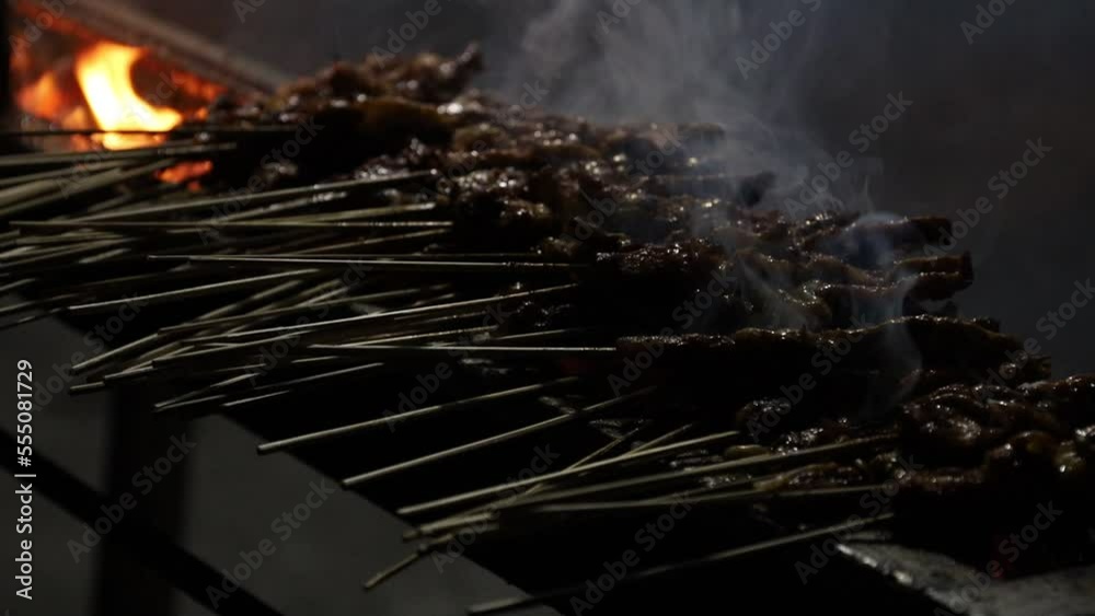 Chicken satay on fire with smoke and an appetizing look. Man hands cooking satay on the grill Chicken satay on fire with smoke and an appetizing look. Man hands cooking satay on the grill