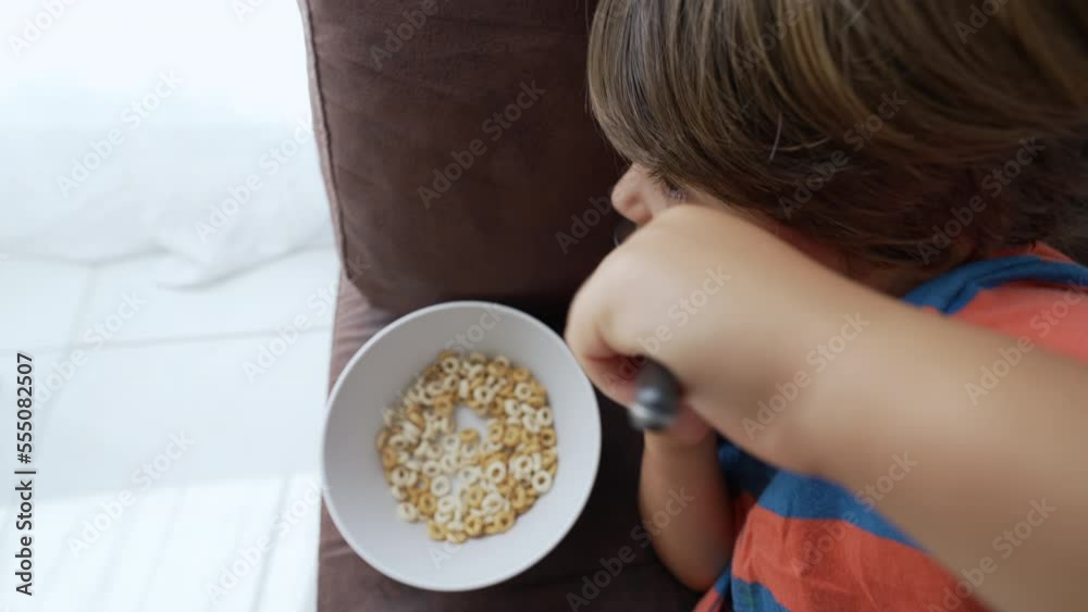 Child eating cereal lying on couch. One little boy eats morning food with spoon Child eating cereal lying on couch. One little boy eats morning food with spoon