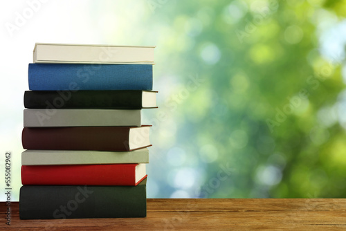 Many stacked hardcover books on wooden table against blurred background, space for text