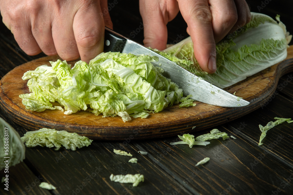 The cook hands are cutting fresh lettuce leaves on a cutting board for vitamin salad. Diet menu for lunch or dinner The cook hands are cutting fresh lettuce leaves on a cutting board for vitamin salad. Diet menu for lunch or dinner