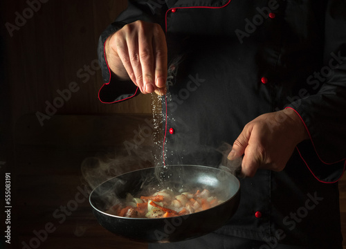 Fototapeta Naklejka Na Ścianę i Meble -  Cooking fresh vegetables. The cook adds salt to a steaming hot pan. The idea of European cuisine for a hotel with advertising space.