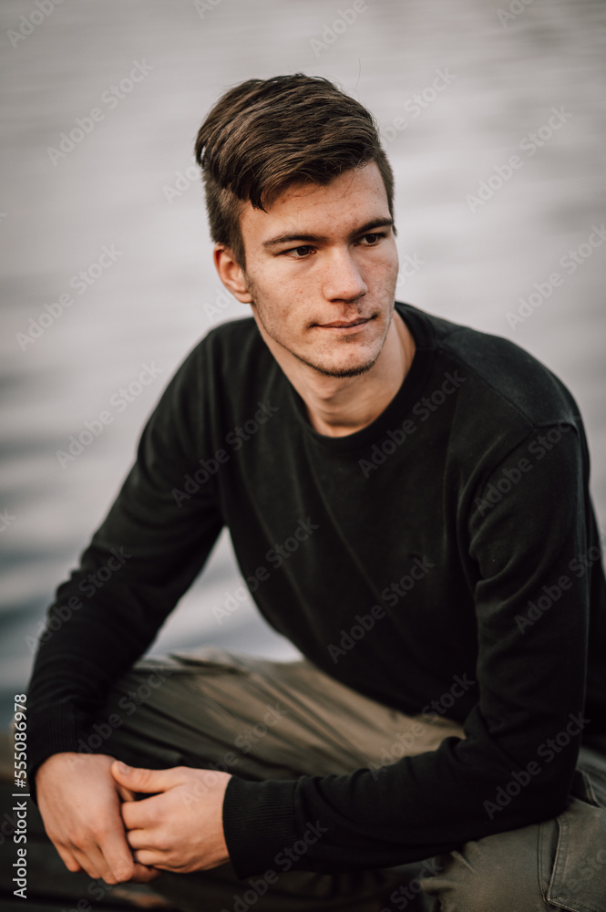 freundliches Portrait ein junger Mann, draußen vor Wasser hockend auf einem Steg. Viel Platz für Text, Quadrat. Mann lächelt in die Kamera freundliches Portrait ein junger Mann, draußen vor Wasser hockend auf einem Steg. Viel Platz für Text, Quadrat. Mann lächelt in die Kamera