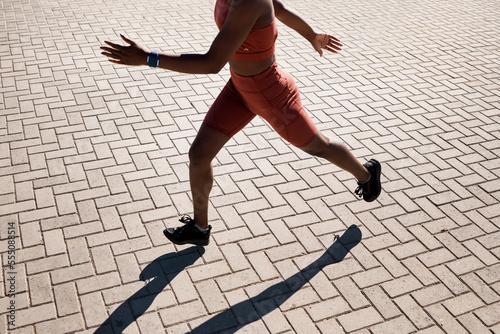 Woman, fitness and running on brick street in sunshine for exercise, cardio workout and marathon training. Closeup legs of runner, athlete and energy with speed, power and action for outdoor sports