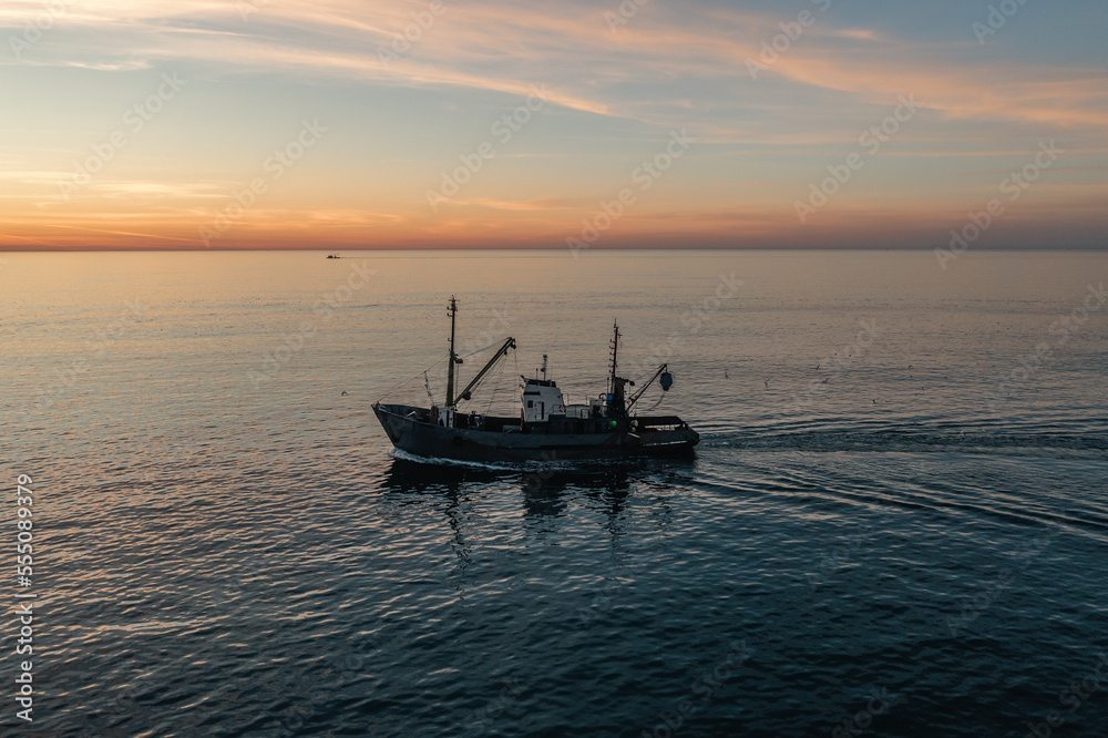 Fishing boat catching fish at sunset aerial view from drone. Small fishing trawler ship on sea surface.