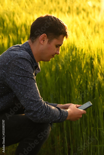 Defocus man with phone on sunset. Young farmer working in a wheat field  inspecting and tuning irrigation center pivot sprinkler system on smartphone. Out of focus
