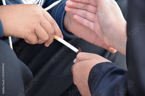 Boys learning to smoke with the same age friends in the area behind the school fence which teachers cannot see  bad influence of secondary school or junior high school life  addiction.