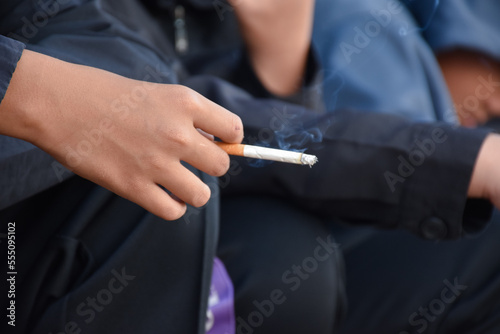 Boys learning to smoke with the same age friends in the area behind the school fence which teachers cannot see  bad influence of secondary school or junior high school life  addiction.