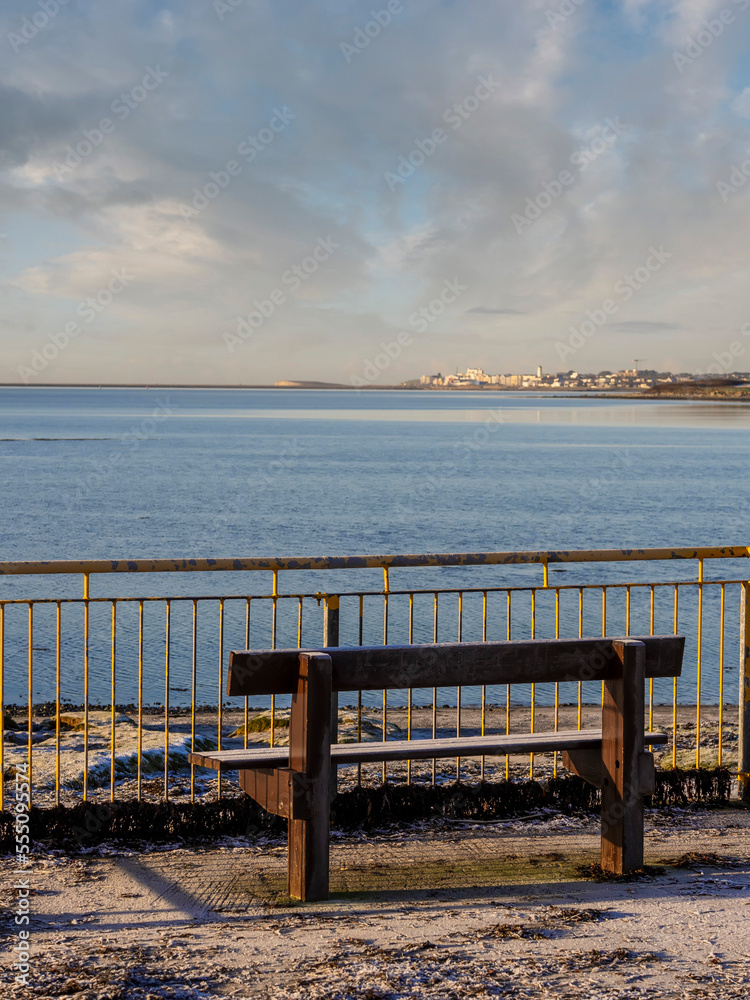 Wooden bench with stunning view on the ocean and town in the background. Blue cloudy sky. Galway city, Ireland. Nobody Wooden bench with stunning view on the ocean and town in the background. Blue cloudy sky. Galway city, Ireland. Nobody