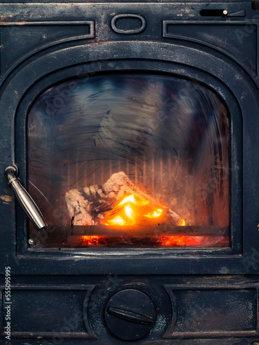 Warm and cozy fire glows in a fireplace. Dirty heatproof glass indicated extensive use during winter months. Keeping house warm concept.