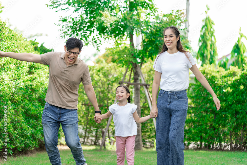 Fototapeta premium Young Asian parents doing activities eating and playing with their daughter in the front yard during the holidays happily.
