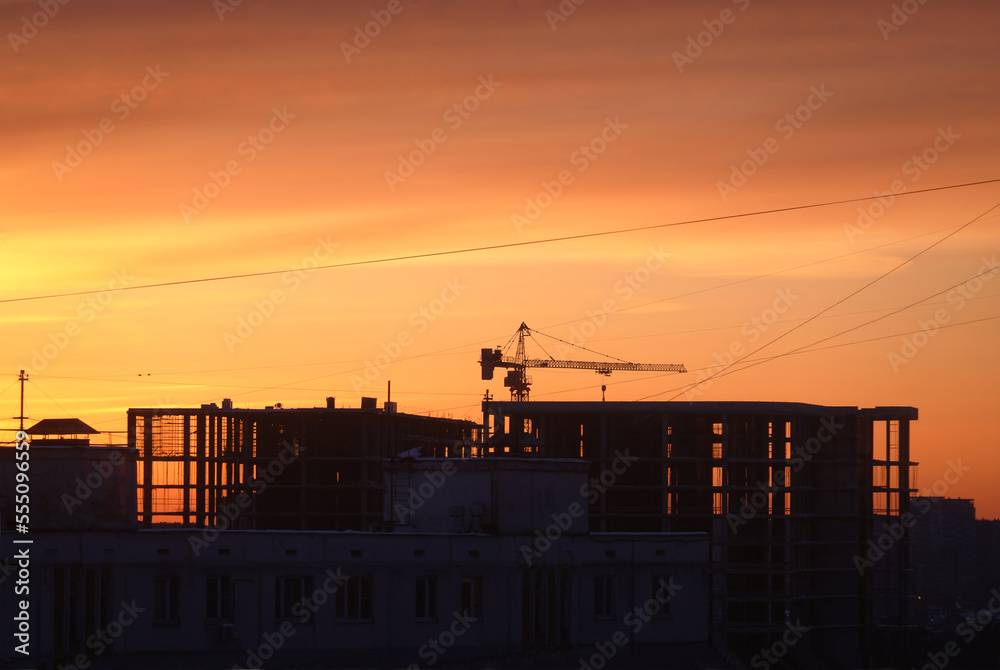 Contour of tower crane above the constructing buildings against cloudless evening sky on the red sunset on the end of workind day