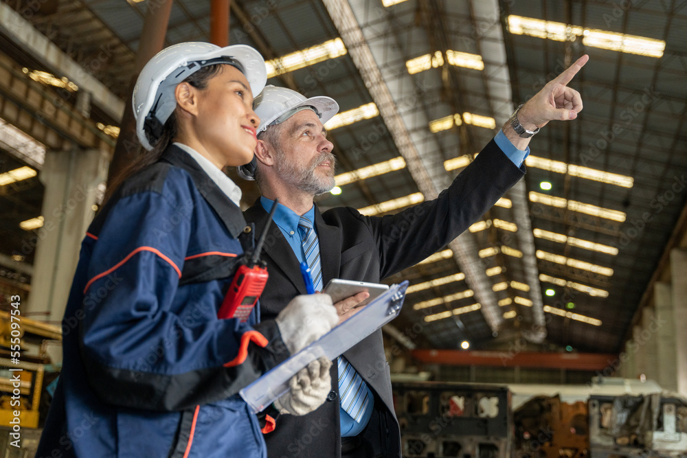 A business man inspects the work of an on-site worker at an old factory for rehearsing train engines. A business man inspects the work of an on-site worker at an old factory for rehearsing train engines.
