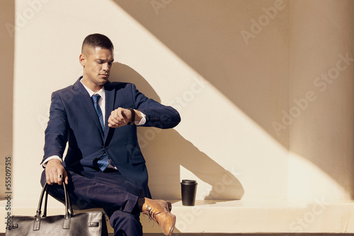 Canvas Print Businessman, city travel or check time while waiting for transport, train or bus in sunshine with leather bag