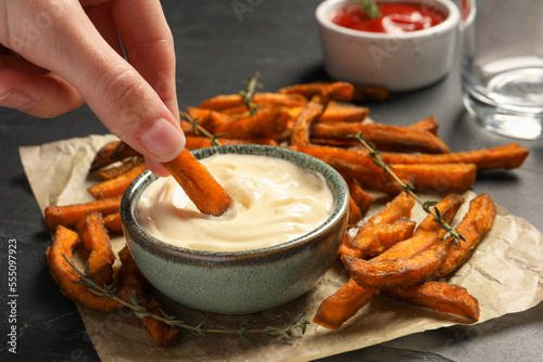 Photos Woman dipping sweet potato fries into sauce at dark grey table, closeup