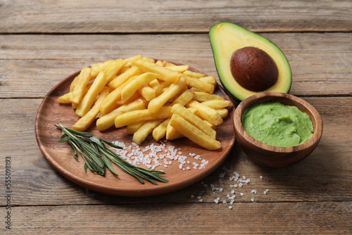 Plate with french fries, guacamole dip and avocado served on wooden table