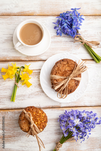 Fototapeta Naklejka Na Ścianę i Meble -  Oatmeal cookies with spring snowdrop flowers bluebells, narcissus and cup of coffee on white wooden background. top view, close up.
