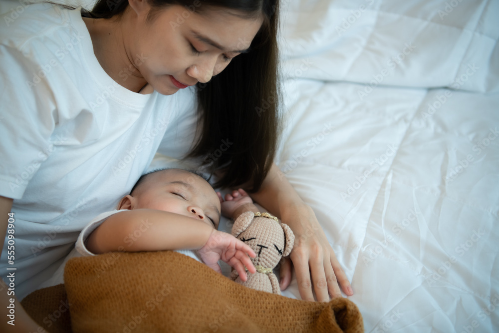 Young mother hugging her newborn child to lull the baby to sleep in the white bedroom Young mother hugging her newborn child to lull the baby to sleep in the white bedroom