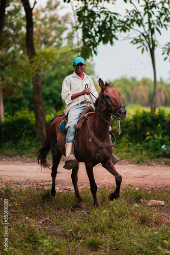 Farm worker rides horse in dirty road with trees © Danilo