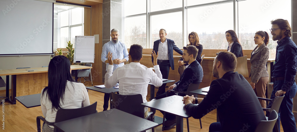 Obraz premium Panoramic view of people office staff standing and sitting at desks in modern office talking during break on corporate team training. Multiracial group men and women discussing seminar or masterclass.