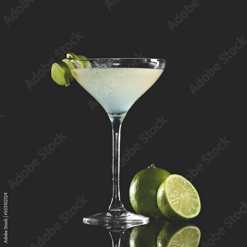 Cocktail Margarita. Alcoholic drink with tequila, lime juice and citrus liqueur. Drink in cocktail glass, decorated with lime, on reflective table. Dark background. Copy space. 