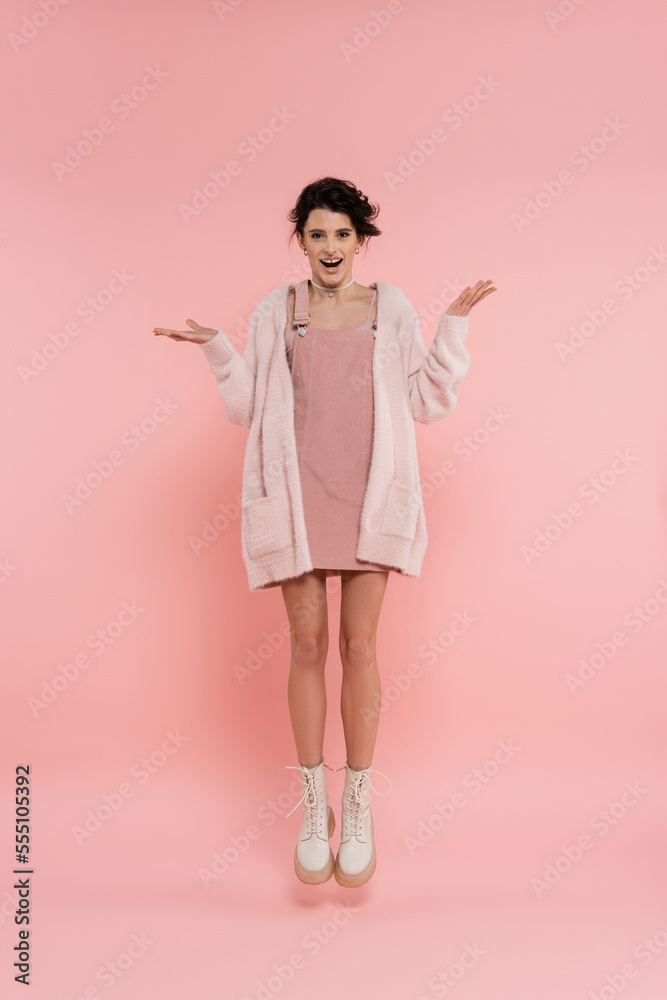 full length of excited woman in strap dress and fluffy cardigan levitating on pink background full length of excited woman in strap dress and fluffy cardigan levitating on pink background