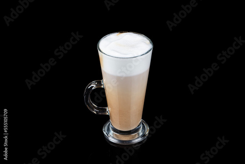 Latte macchiato in beautiful cup on wooden background with natural shadow. Cappuccino frothy coffee and milk drink in clear glass cup. Chai Latte pouring shot. Chai Latte Drink.