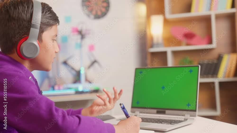 kid making notes from online class on green screen laptop at home - concept of e-learning, intelligence and education