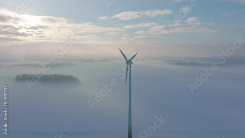 Establishing aerial view of wind turbine generating renewable energy in the wind farm, snow filled countryside landscape with fog, sunny winter day, wide drone shot moving forward photo