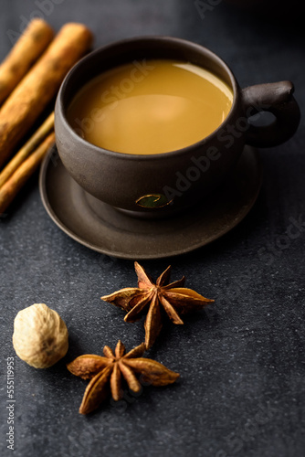 Masala tea in a clay mug and teapot. Traditional Indian hot drink with milk and spices on dark background