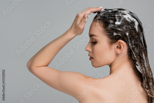 side view of young woman with closed eyes washing wet and foamy hair isolated on grey
