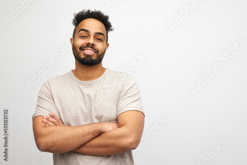 Portrait of happy Jamaican man looking handsome isolated on caramel and beige colored background, placed in the left side with room for copyspace and with arms crossed.