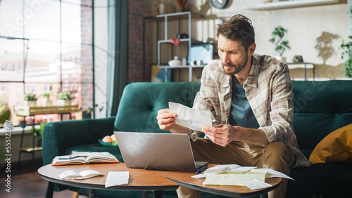 Accounting at Home: Streessed Man Using Laptop Computer, Filling Tax Forms. Businessman Scared of Bankruptcy. Paperwork Problems: Bills, Invoices, Budget Deficit, High Inflacion, Financial Difficulty photo