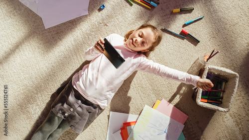 Top View Home: Happy Little Girl Using Smartphone While Lying on the Floor. Joyful Sunny Day and Clever Smiling Child Playing Smart Video Games, Using e-Learning Apps on Mobile Phone.