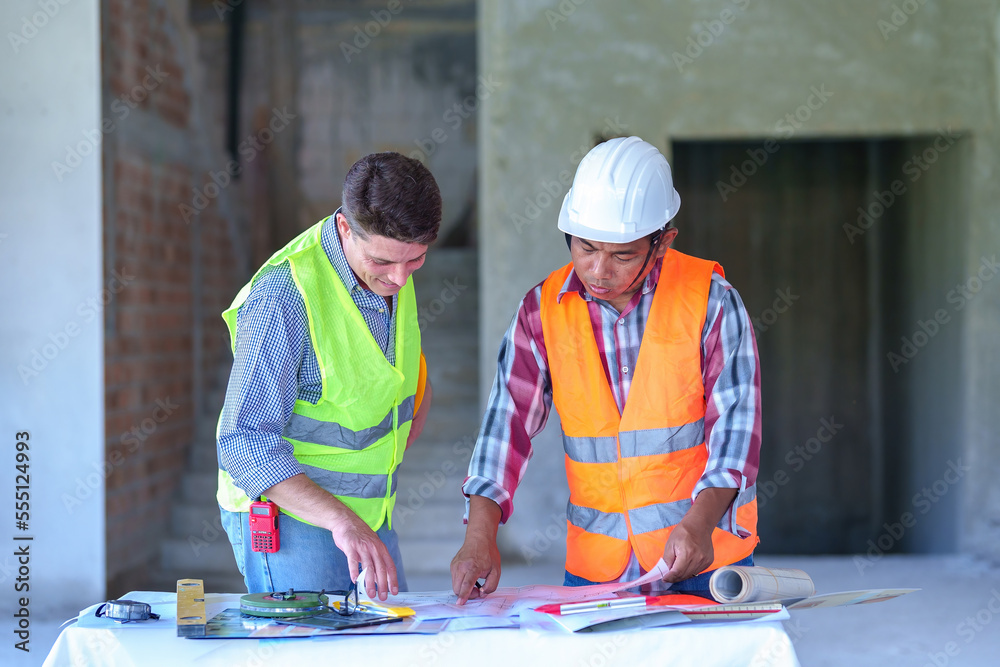 Two construction engineers holding blue print and inspecting the construction site Two construction engineers holding blue print and inspecting the construction site