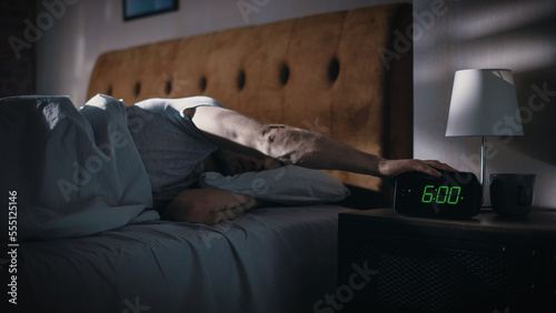 Man Wakes Up, Turns off Alarm Clock with Frustration, after Sleepless Insomniac Night. Early Rising Stressed Man Ready to Face Day of Problem Solving. Focus on the Clock Showing Six A.M.